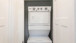 A laundry room with a stacked washer and dryer, white doors, and a wooden floor. - Jeffreys Bay - Loft #3 - 8 min walk to beach (Virginia Beach)