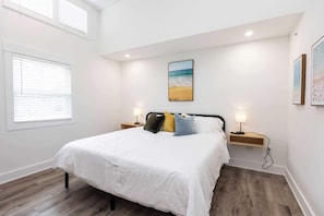 A bedroom with a bed, two bedside tables, a wall-mounted picture, and a window with blinds.