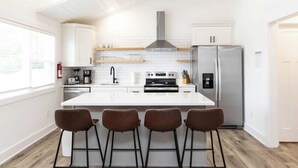 A modern kitchen with a central island, bar stools, a stainless steel refrigerator, and a built-in oven. - Jeffreys Bay - Loft #3 - 8 min walk to beach (Virginia Beach)