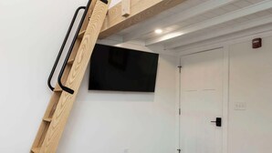 Ett rum med en säng på ett loft, en stege, en platt-TV och en dörr.