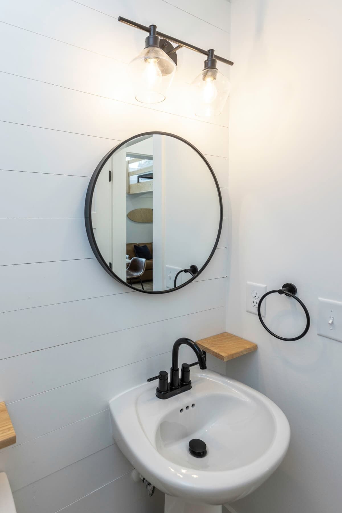 Un baño con un lavamanos blanco, un espejo redondo y un aro para toallas.
