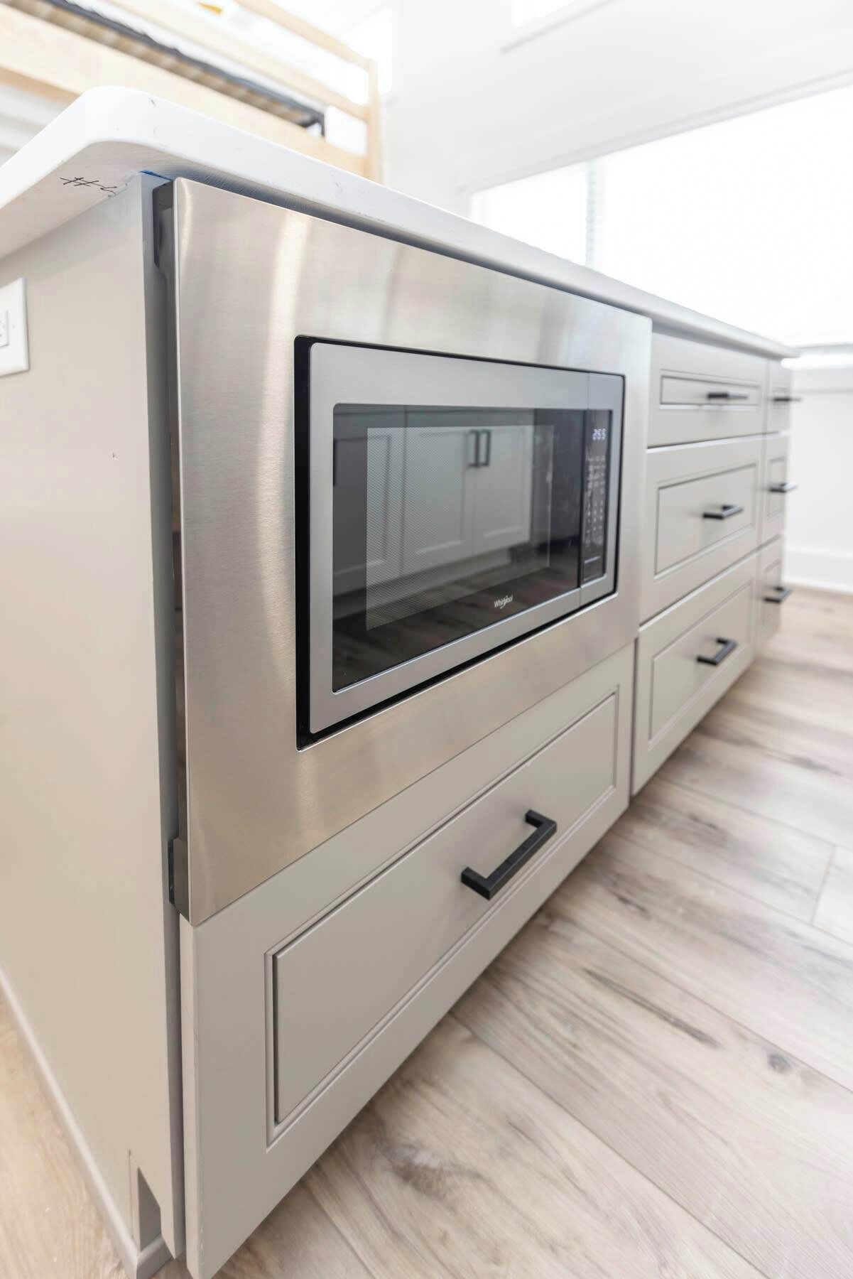 A stainless steel microwave oven integrated into a kitchen cabinet with drawers.
