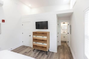 A bedroom with a wooden dresser, a flat-screen TV, and a white door. - Jeffreys Bay - Loft #3 - 8 min walk to beach (Virginia Beach)