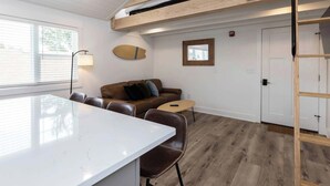 A modern living space with a white kitchen island, a brown leather sofa, and a wooden loft bed. - Malibu - Loft #4 - 8 min walk to the beach (Virginia Beach)