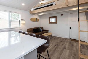 A modern living space with a white kitchen island, a brown leather sofa, and a wooden loft bed.