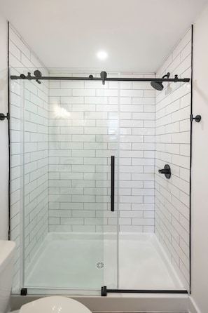 A glass-enclosed shower with white tiled walls and a glass door.