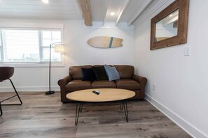 A modern living room with a brown leather sofa, a round wooden coffee table, and a floor lamp. - Malibu - Loft #4 - 8 min walk to the beach (Virginia Beach)