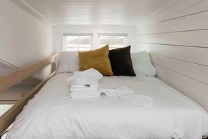 Un dormitorio con una cama, dos ventanas y un cabecero de madera.