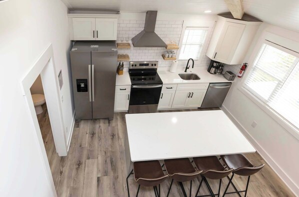 Una cocina compacta con refrigerador, estufa, lavaplatos y un comedor con taburetes.