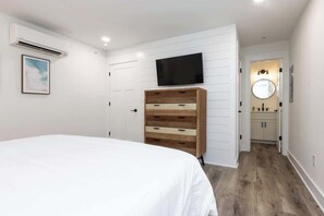 A bedroom with a bed, a dresser, a television, and a bathroom with a mirror and sink.