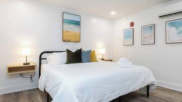Une chambre à coucher avec un lit, des lampes de chevet, une étagère fixée au mur et un tableau sur le thème de la plage.