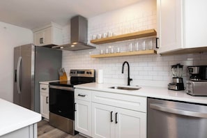 A modern kitchen with stainless steel appliances, white cabinetry, and a wooden shelf above the sink. - Rincon - Loft #6 - 8 min walk to the beach (Virginia Beach)