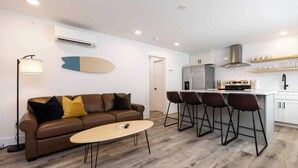 Een moderne woonkamer met een bruine leren bank, een ronde salontafel en een keuken met een witte koelkast, kookplaat en barstoelen.