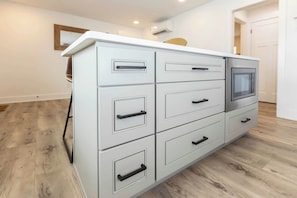 A white cabinet with drawers and a microwave, wooden flooring, and a white door in the background. - Rincon - Loft #6 - 8 min walk to the beach (Virginia Beach)