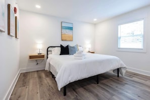 A bedroom with a bed, bedside lamps, a nightstand, a window with a view, and a framed picture on the wall.