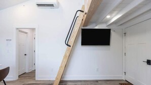Una habitación con una escalera de madera, un televisor de pantalla plana montado en la pared y una puerta que da a otra estancia.