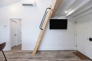 Ein Zimmer mit einer Holztreppe, einem an der Wand befestigten Flachbildfernseher und einer Tür zu einem weiteren Raum.