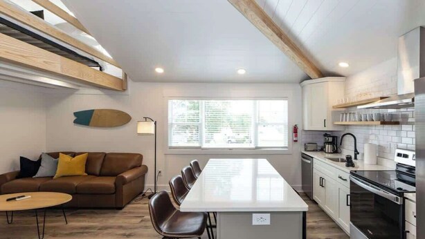 Una cocina moderna con una isla central, una zona de comedor con un sofá de cuero marrón, y un ventanal que proporciona luz natural.