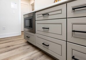 A kitchen with a microwave, multiple drawers, and a wooden floor.