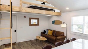 Una habitación estilo loft con una cama litera, un comedor y una zona de estar con sofá y sillas.