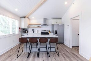 Eine moderne Küche mit Kochinsel, Barhocker und einem Edelstahlkühlschrank.