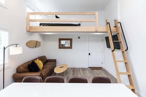 Ein Zimmer mit einem Etagenbett, einer Schlafcouch, einem kleinen Tisch und einer Stehleiter.