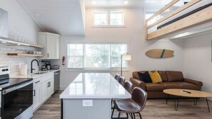 Une cuisine moderne avec des meubles blancs, un îlot central et un coin repas comprenant un canapé en cuir marron et une petite table ronde.