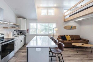 A modern kitchen with white cabinets, a central island, and a dining area with a brown leather couch and a small round table.