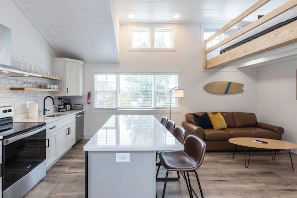 A modern kitchen with white cabinets, a central island, and a dining area with a brown leather couch and a small round table.