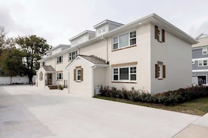 A multi-story residential building with a flat roof, a front entrance with steps, and a driveway.