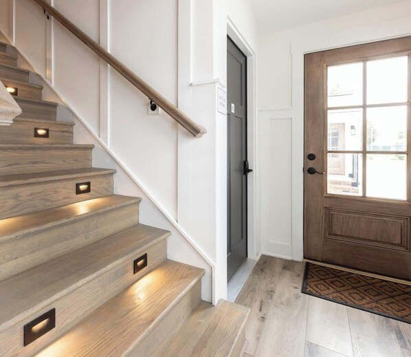 A staircase with built-in lighting, a door with a window, and a patterned doormat.