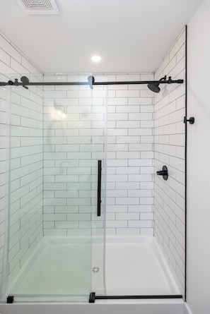 A glass-enclosed shower with white tiled walls and a black handle.