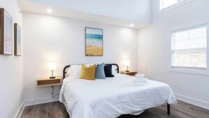 Une chambre à coucher avec un lit, des lampes de chevet, une table de chevet, un tableau accroché au mur et une fenêtre.