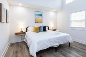 A bedroom with a bed, bedside lamps, a nightstand, a wall-mounted painting, and a window.