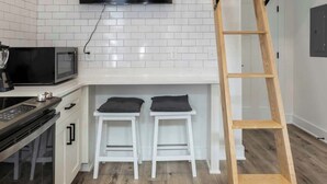 A modern kitchen with a TV, white cabinets, a microwave, and a wooden floor. - Pipeline - Loft #9 - 8 min walk to the beach (Virginia Beach)