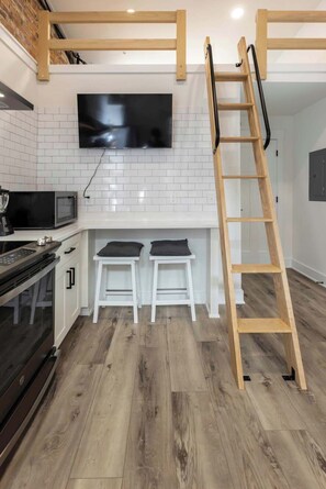 Eine moderne Küche mit Fernseher, weißen Schränken, einer Mikrowelle und Holzboden.