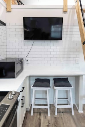 Una cocina equipada con microondas, estufa y televisor montado en la pared.