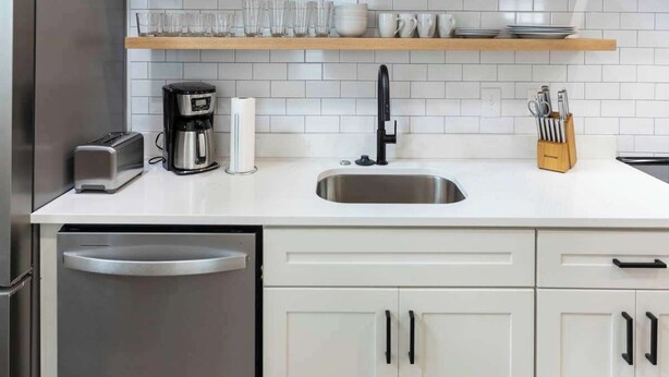 A modern kitchen with white cabinets, a stainless steel dishwasher, a coffee maker, and a sink. - Pipeline - Loft #9 - 8 min walk to the beach (Virginia Beach)
