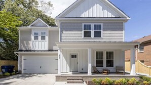 Une maison à deux étages avec un porche à l’avant, un garage et une allée pavée en briques.