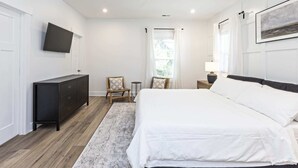 Une chambre à coucher comprenant un lit, une commode, une chaise, une table de chevet, une lampe, un ventilateur de plafond et un téléviseur fixé au mur.
