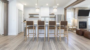 Une cuisine moderne avec des meubles blancs, un îlot central doté de tabourets et une cheminée en briques.