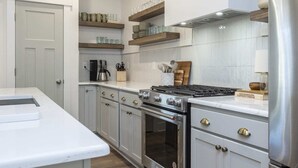 Une cuisine moderne avec des meubles blancs, des appareils en acier inoxydable et des étagères en bois.