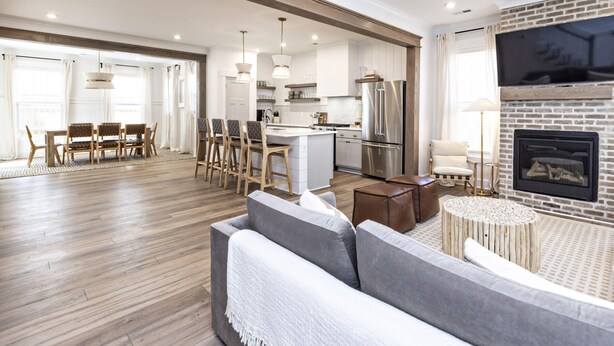 Un vaste espace de vie comprenant un canapé, une table à manger et des chaises. Il y a également une cuisine équipée d’un réfrigérateur et d’une cheminée.