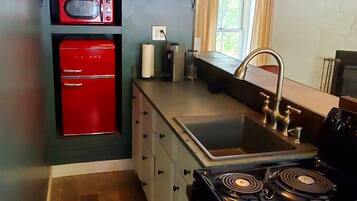 A compact kitchen with a red refrigerator, a microwave, a stove, and a sink.