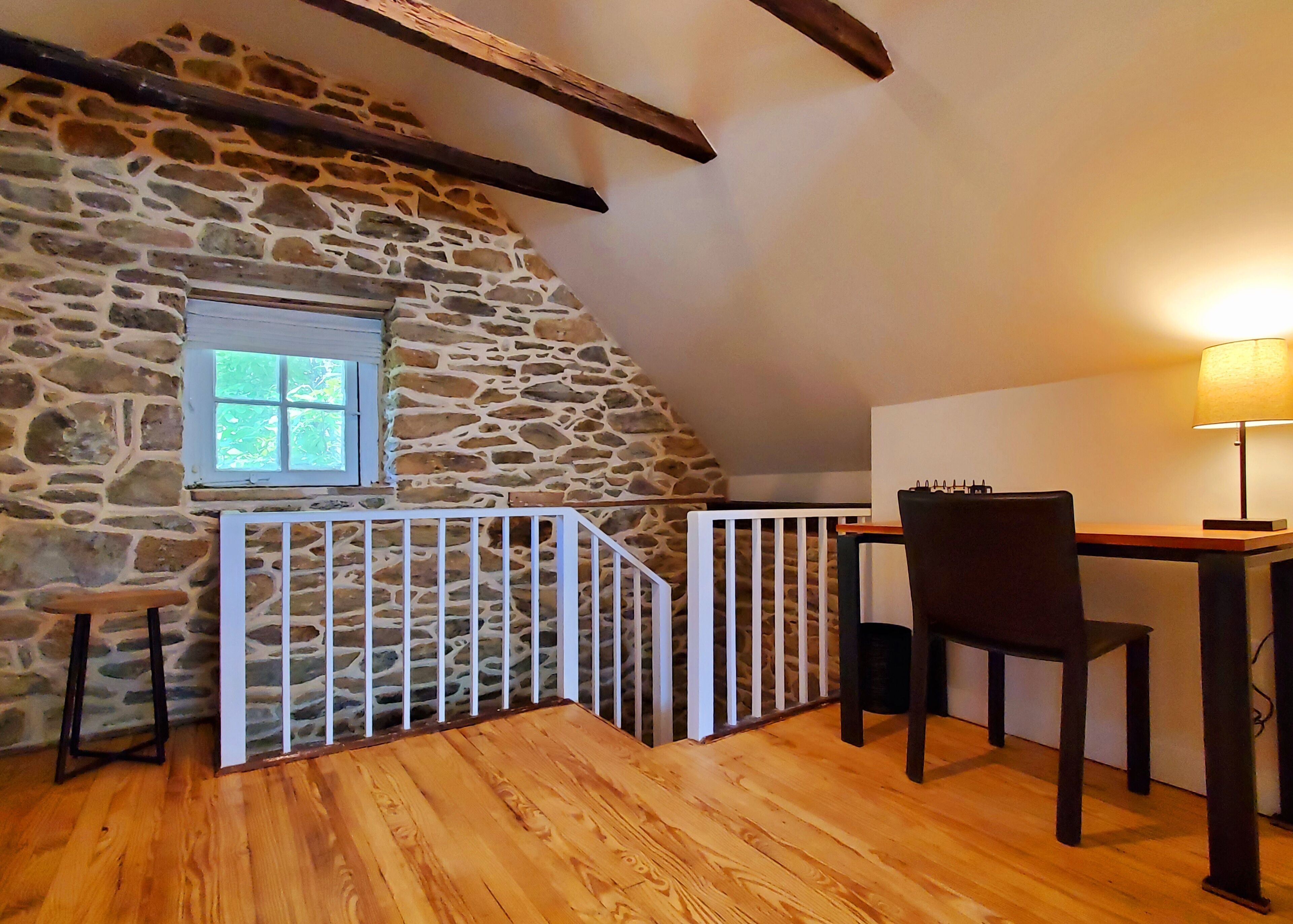 A cozy room with a stone wall, a wooden desk, a chair, and a small window.