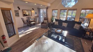 Un salon spacieux avec un canapé aux couleurs sombres, une table basse en verre et un coin repas comprenant une table et des chaises en bois.