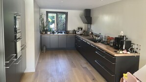A modern kitchen with grey cabinets, a wooden countertop, and a window providing natural light. - Charmante Maison Familiale (Gradignan)