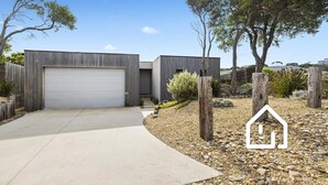 A modern two-story house with a garage, surrounded by a gravel driveway and landscaped garden.