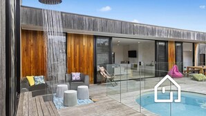 A modern house with a wooden exterior, a glass-enclosed pool, and outdoor seating.