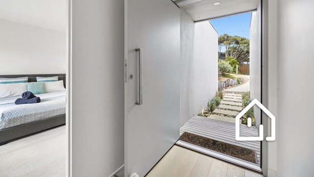A modern bedroom with a bed, a bedside table, and a view of the garden through a glass door.
